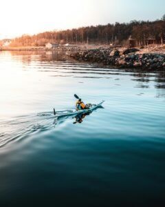 Kayaker paddles across calm waters near a rocky shoreline, perfect for a tranquil outdoor adventure.
