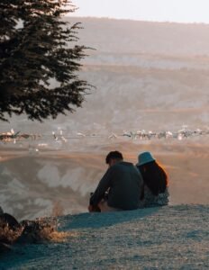 A couple sits on a hill overlooking the scenic landscapes of Cappadocia, Türkiye at sunset.